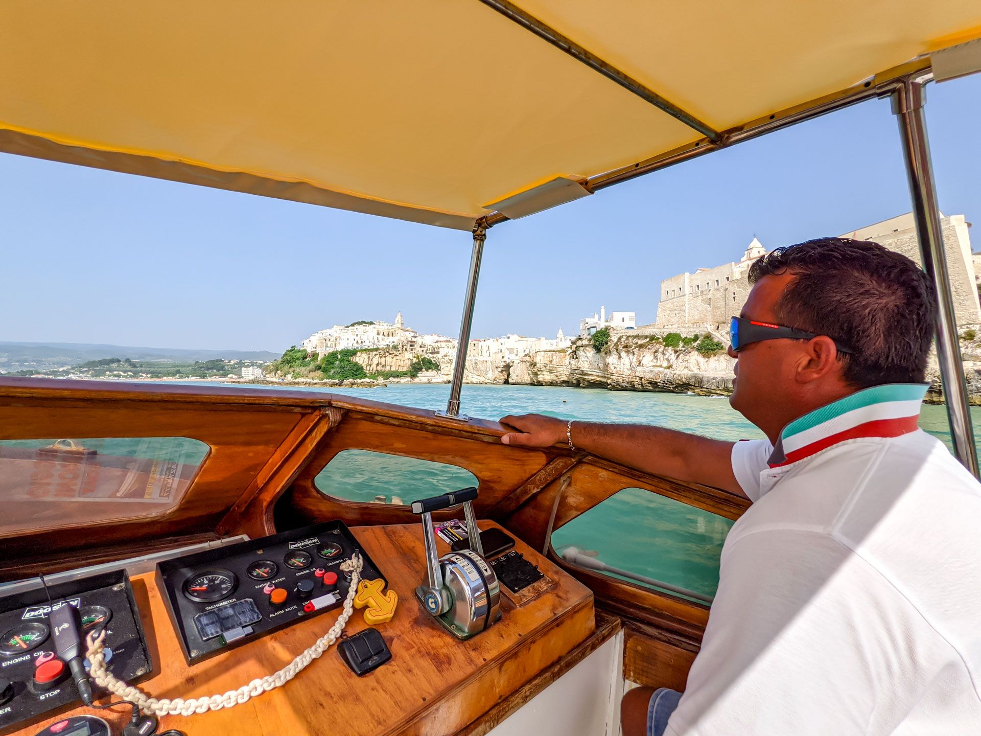 capitano guida la barca di fronte al centro storico di Vieste durante escursione Motobarche Leonarda